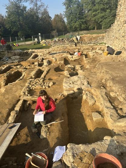 Scavi archeologici nel Parco Archeologico di Castelseprio, con una ricercatrice che prende appunti mentre lavora in un'area di scavo.