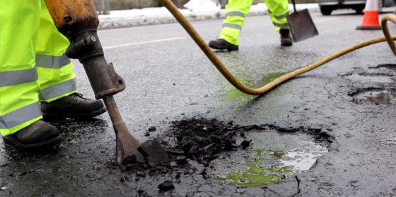 Road maintenance worker using asphalt to fill a pothole on a local road.