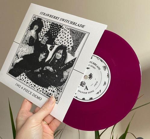 A hand holds the cover of Strawberry Switchblade's 1982 4 Piece Demo E P, with the record half sticking out in a luscious purpley-pink colour