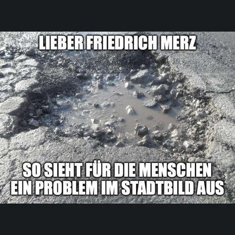 Ein Schwarzweißfoto zeigt einen Teil eines Bürgersteigs mit einer großen, unregelmäßigen Beschädigung. Die Beschädigung ist kreisförmig und besteht aus zahlreichen zerbrochenen Steinen, die sich nach innen verengen. Im Zentrum der Beschädigung befindet sich eine kleine Ansammlung von Wasser oder Schlamm. Um die Beschädigung herum ist der Bürgersteig mit unregelmäßigen Steinen gepflastert. Oben im Bild steht in Großbuchstaben der Text "LIEBER FRIEDRICH MERZ" und unten der Text "SO SIEHT FÜR DIE MENSCHEN EIN PROBLEM AUS".