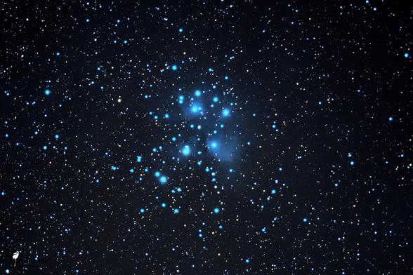 A photo of a small section of the night sky. It contains a few larger, very bright bluish stars and a lot of other white, yellow, and blue stars. Blue nebulae surround the larger stars.