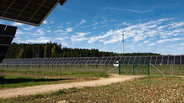 In der direkten Nachbarschaft zum großen AgriPV-Park steht das Veringstädter Wind-Rad. Ebenfalls in Bürger:innen-Hand. Auf dem Bild zu sehen sind im Vordergrund die Solar-Panele. Aus dem Wald am Horizont ragt das Wind-Rad hervor.