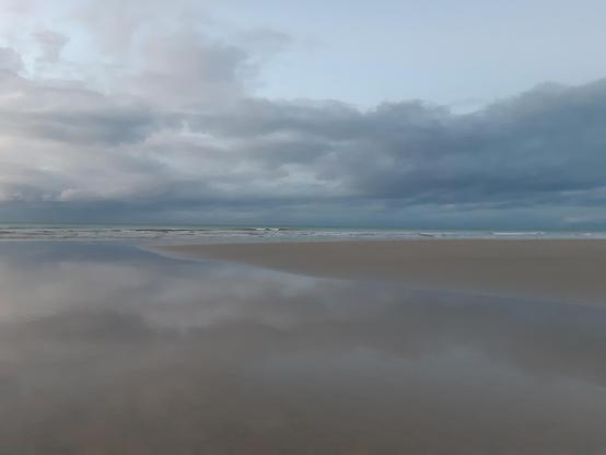 L'image est coupée en deux par la ligne d'horizon,
Le ciel nuageux surplombe une plage aux couleurs pastel, on dirait un paysage d'aquarelle