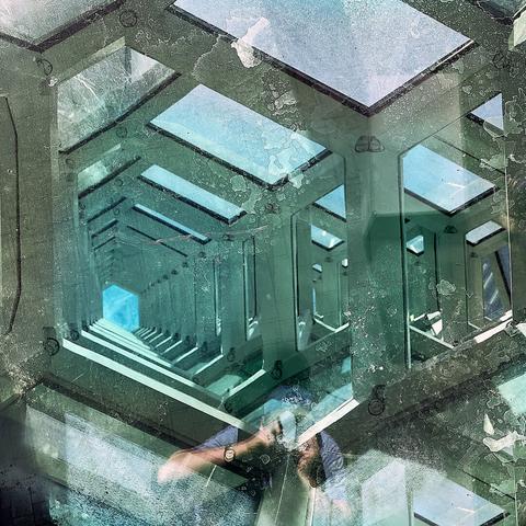 The image shows a reflective surface capturing a pattern of geometric shapes. It has multiple green-tinted, rectangular frames layered on each other, creating a tunnel-like effect. The reflection also includes the faint outline of a person holding a camera