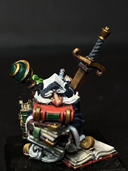 Gnome Faimilar/Wizard in deep Blue robes, a seeped twice his height is sheathed on his back, and he is carrying a plethora of books.