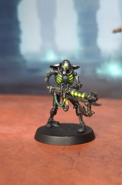 A painted Warhammer mini. A Necron Warrior with glowing green weapons and chest and silver body.