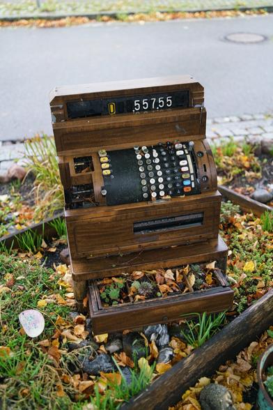 Jemand hat eine alte Registrierkasse aus Holz ins Beet gestellt