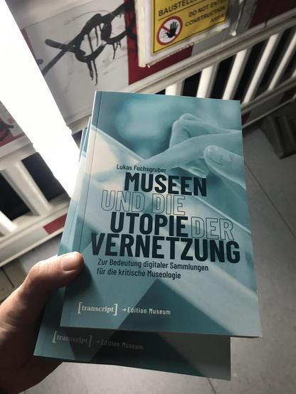 Eine Hand hält 2 Exemplare des  Buchs Museen und die Utopie der Vernetzung