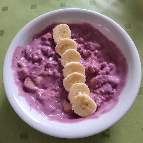 Pinkes Dinkel-Beeren-Müsli, mit Zimt und Bananen. Es ist in einer schlichten, weissen Schale und steht auf einem grasgrünen Tischtuch.