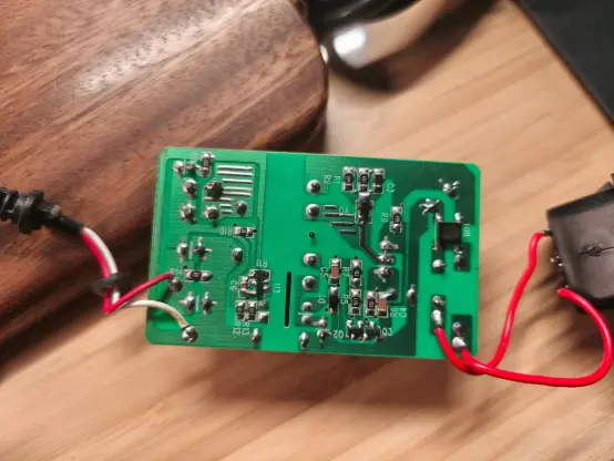 Eine grüne Platine mit zwei dünnen roten Kabeln rechts, wo 220V rein gehen sollen und Kabel gleicher stärke auf der linken seite, in rot und weiß. Das weiße ist vermutlich durchs Löten ein wenig angesengt.