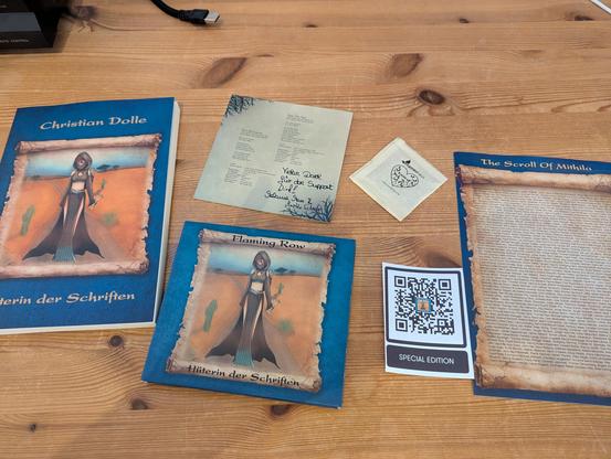 Wooden Desk with a book, digipack, CD booklet with personal note, a small bag of cress seed, and a single page "The Scroll Of Mithila" with what appears to be names of all supporters.