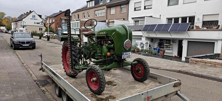 Grüner alter Traktor von rechts vorne. Man sieht sehr präsent den Mähbalken in Parkposition (hochkant).
