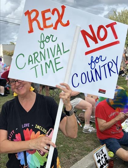A protester at the October 18,2025 NO KINGS rally carries a hand-painted sign that reads, “REX for Carnival Time, NOT for Country.”