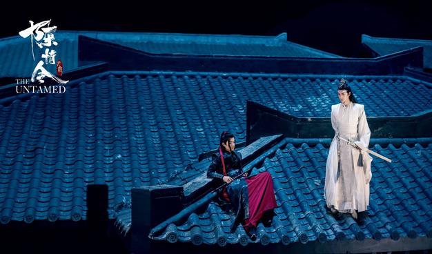 Wei Wuxian reclines on a roof at night in Qinghe. Lan Wangji stands nearby.