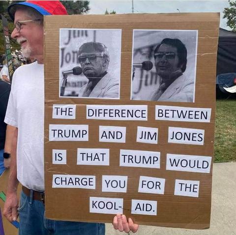guy holding up a sign wtih pics of trump(with jim jones glasses on) and jim jones and it says

The difference between trump and jim jones is that trump would charge you for the kool-aid
