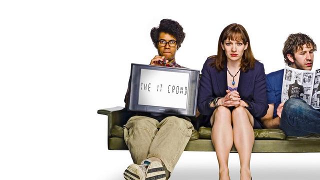 Drei Personen sitzen auf einer Bank. Die linke mit eigentümlicher Frisur und Nerd-Brille hält einen Monitor mit der Aufschrift "IT-Crowd". In der Mitte sitzt eine etwas verzweifelt schauende weiblich gelesene Person im Business-Outfit. Rechts liest eine Person konzentiert einen Comic. Die drei sind Potagonisten der US-Serie IT-Crowd.