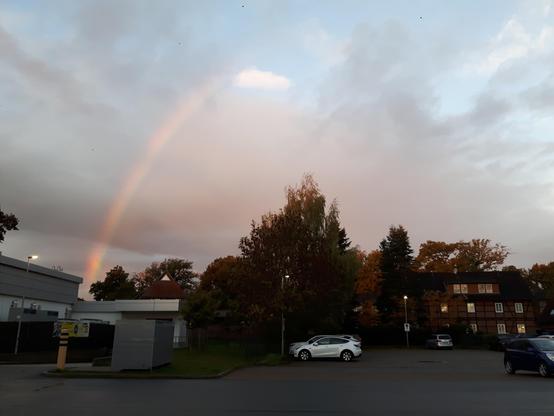 Fotos eines Stück eines Regenbogens über einem Parkplatz. Der linke Fußteil des Bogens ist zu sehen, er steigt sehr steil auf.