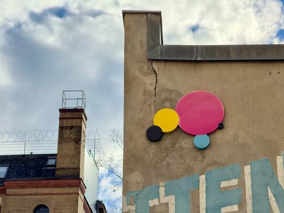 Kreise an einer Häuserwand in den Farben Cyan, Magenta, Gelb und Schwarz.