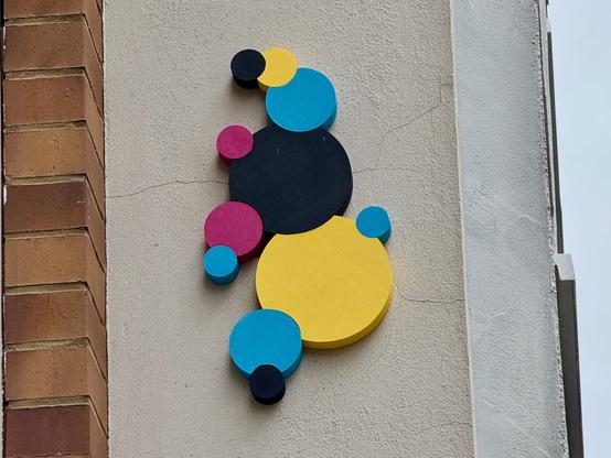 Kreise an einer Häuserwand in den Farben Cyan, Magenta, Gelb und Schwarz.