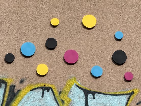 Kreise an einer Häuserwand in den Farben Cyan, Magenta, Gelb und Schwarz.