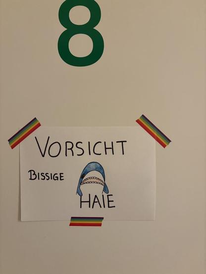 Bild einer weißen Tür mit einer großen, grünen, aufgedruckten „8“.
Unter der Acht hängt ein Zettel auf dem mit großen Buchstaben steht: „Vorsichtig. Bissige Haie“ über dem Wort „Haie“ schaut ein gezeichneter Blåhaj hervor.
Der Zettel ist mit Regenbogentape an der Tür befestigt.