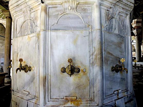 Foto van messing kranen voor rituele wassing aan wit marmeren, zeskantige constructie