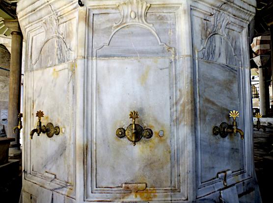 Foto van messing kranen voor rituele wassing aan wit marmeren, zeskantige constructie