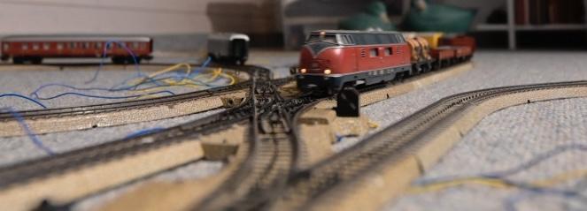 Eine rote modelleisenbahnlokomotive fährt auf dich zu während er eine Weichenstrasse überquert