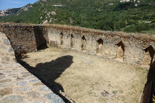 un mur de pierres dans lequel sont ménagées des niches de 2m de haut, 40 cm de profondeur. La partie supérieur de la niche n'est pas une arche, mais constitué de deux pierres posées perpendiculairement. Derrière, le maquis, tout vert ( photo prise en mai) et les arbres qui caractérisent la Balagne. On y voit, au milieu, le cimetière de Corbara, à gauche, Corbara, et à droite, le couvent Saint Dominique