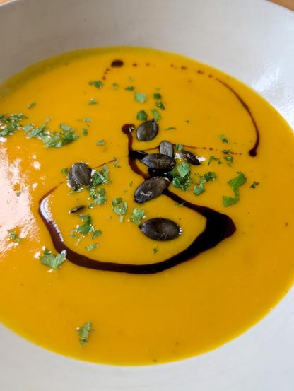 Cremige, orangefarbene Kürbissuppe in einem weißen Teller, dekoriert mit Kürbiskernen, frischer Petersilie und einem Ring Kürbiskernöl. Foto by Johann Seidl, Gartenpoet.