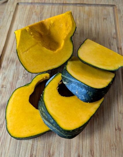 Aufgeschnittener Kürbis der Sorte Uncle David’s Dakota Dessert auf einem Holzbrett, kräftig orangefarbenes Fruchtfleisch mit dunkelgrüner Schale. Foto by Johann Seidl, Gartenpoet.