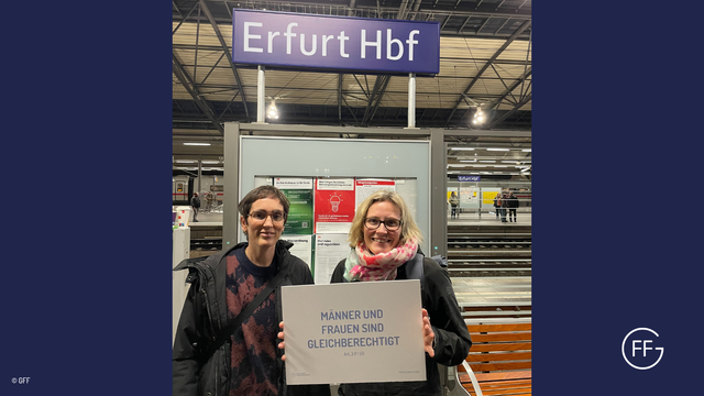Sarah Lincoln und Maria Scharlau stehen am Erfurter Hauptbahnhof. Maria hält ein Schild in den Händen. Darauf steht: Männer und Frauen sind gleichberechtigt. Art. 3 II 1 GG