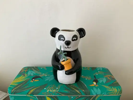 Small vase shaped as a panda holding a potted (light blue-green) plant with 3 leaves.