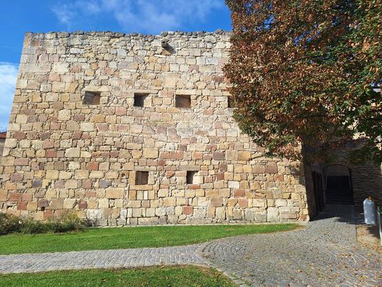 Eine Stadtmauer, davor ein Rasen und ein gepflasteter Weg.