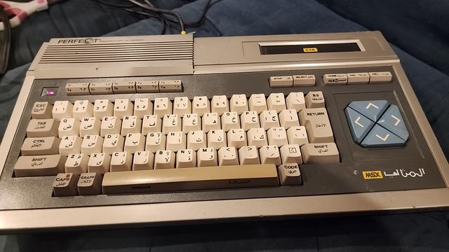 a Daewoo MSX-1 "perfect" (المثاليا) microcomputer. there is a cartridge slot at the top right, a row of function keys, a qwerty keyboard with nearly the same as modern Arabic-101key layout (ضصثقفغ) and  directional keys to the right of the keyboard.