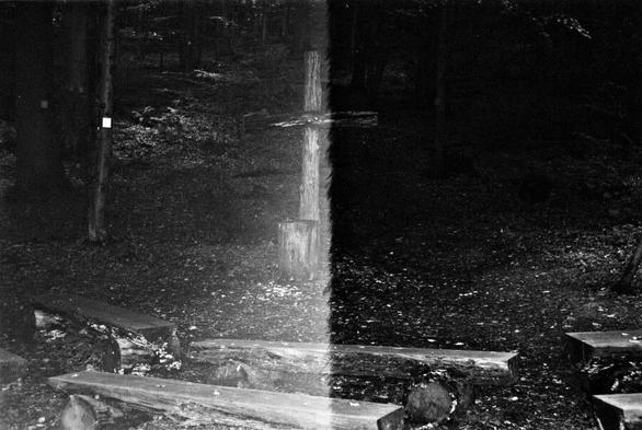 A rotting wooden cross in front of some benches. Half of the image has a weird artifact from a misfired flash or mistimed shutter.