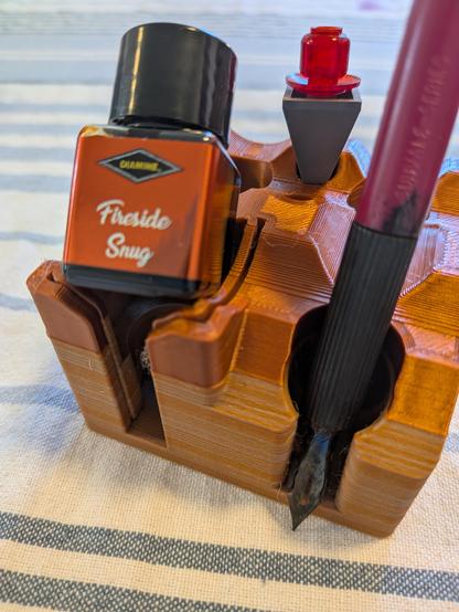 A bottle of Fireside Snug ink which is a reddish orange, with a dip pen, and a Lego navigation marker.