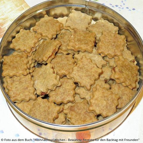 Auf dem Tisch eine Blechdose mit braunen gefüllten Kaffeeplätzchen.