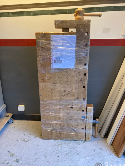 Ovansida på en inplastad snickarbänk på högkant lutad mot en vägg.