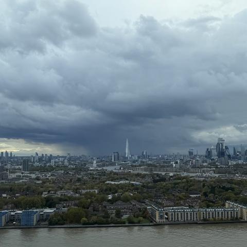 A photo of some very dark and angry looking skies over London this afternoon. Facing west, towards The Shard, we can see the Thames looking murky in the foreground. In the mid ground, we see the Shard, framed against the impressive looking clouds and what looks like some very heavy rain in the distance. Photo taken from a high-rise apartment building in Canary Wharf in the east of London.