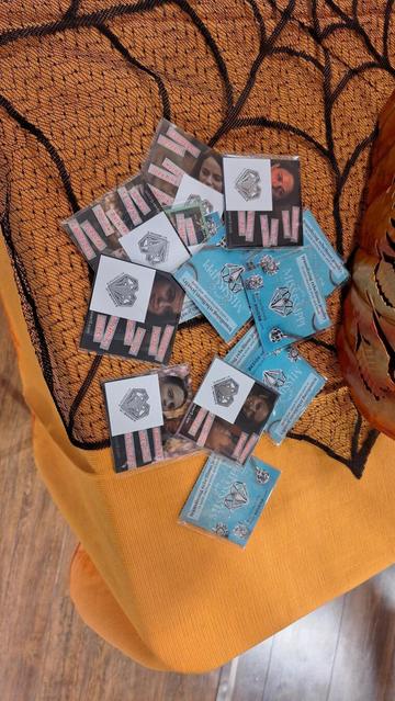 Xover0 stickers and temporary tattoos rest on a table with an orange and black spiderweb table cloth. 
~
Xover0-stickers en tijdelijke tatoeages liggen op een tafel met een oranje en zwart spinnenweb-tafelkleed.
~
Des autocollants et des tatouages temporaires Xover0 reposent sur une table recouverte d’une nappe orange et noire à motif de toile d’araignée.