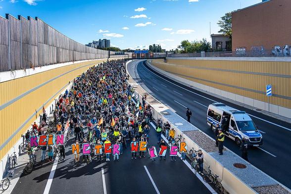 Das Foto zeigt die Demo auf der A100. In der vorderen Reihe tragen Menschen große Pappbuchstaben, die den Satz: "Kein Meter weiter" ergeben.