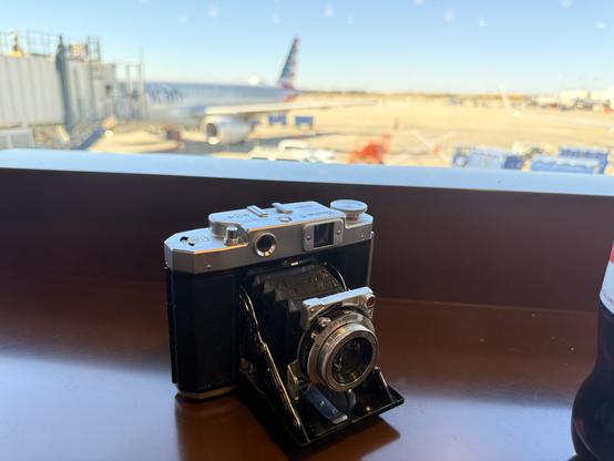 A Mamiya 6 folder, splayed out in all its glory with an out of focus view behind out a window looking at the airport tarmac and a plane at the gate
