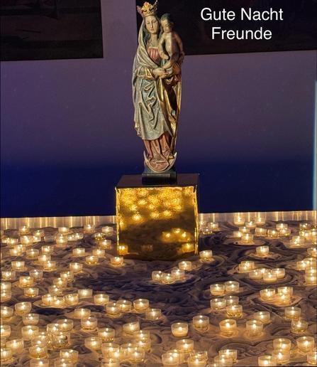 Eine Madonnenfigur steht auf einem Post inmitten eines Meeres kleiner brennender Lichter