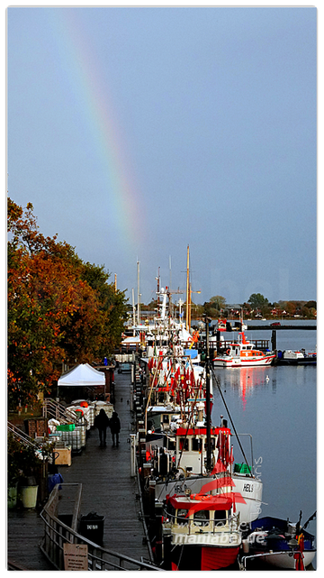 Fischkutter liegen im Hafen in einer Reihe. Am Ende der Reihe ein Regenbogen.