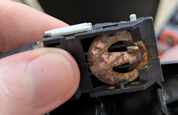a bottom view of the switch, showing that the black plastic part has a circular metal piece inside of it. I think the white metal part presses into this with a little "beak" when the switch is in the on position

the metal piece is covered in a ton of rust, and the tip of the "beak" has some rust too