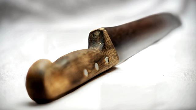 Das Bild zeigt ein altes Messer mit Holzgriff auf weißen Untergrund. Der Griff ist von der Benutzung leicht speckig. Der Focus liegt in der Mitte. Die Klinge verschwimmt im Hintergrund  und der Griff im Vordergrund.