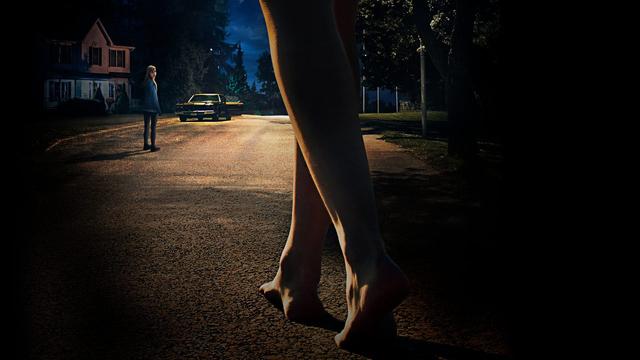 "It Follows": Jay (Maika Monroe) steht im Hintergrund nachts auf einer einsamen Straße. Im Vordergrund sind zwei nackte Füße zu sehen, die auf sie zugehen. Bild: © ZDF/IT WILL FOLLOW, INC