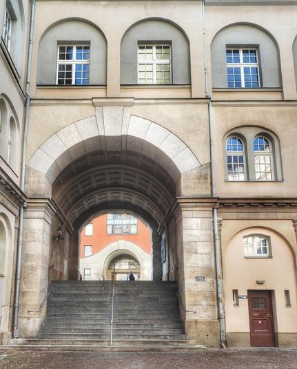 Ein Torbogen im Rathaushof mit einer Treppe, die zu einer Straße führt, darüber und rechts davon Fenster. Unter dem rechten Fenster eine kleine verschlossene Tür.