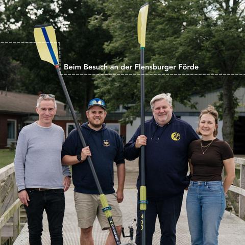Gruppenfoto vom Projekt reday2race: Vier Personen schauen stehen nebeneinander und schauen in die Kamera. Zwei Personen halten Ruder in den Händen Richtung Himmel.